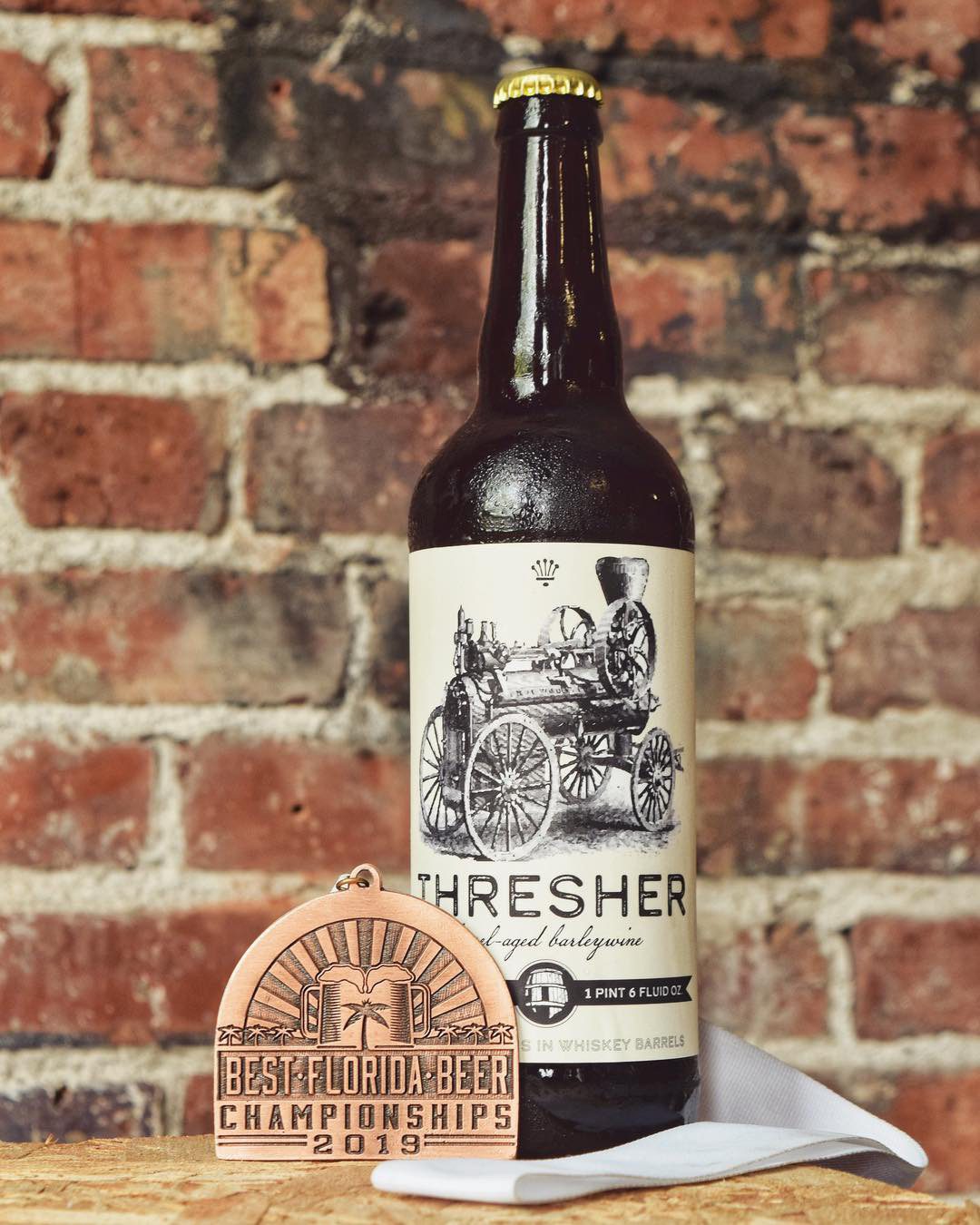 Thresher English-Style Barleywine in bottle in brewhouse in front of brick wall