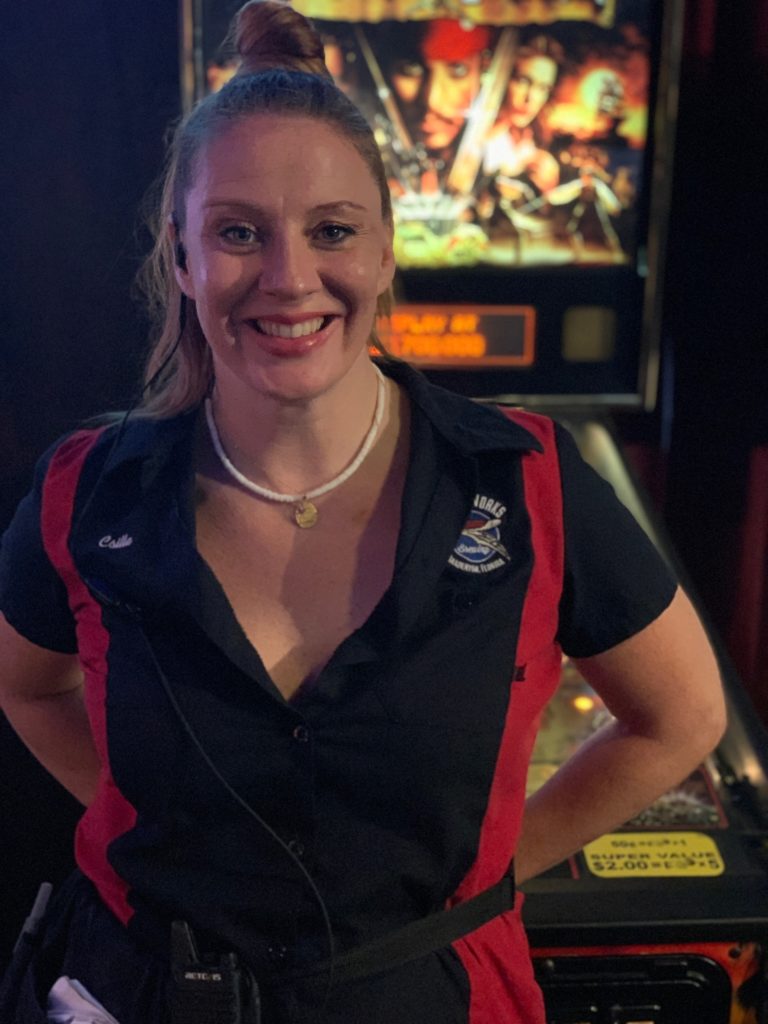 Motorworks Brewing Crew Photo - Csilla Petofi in front of pinball machine