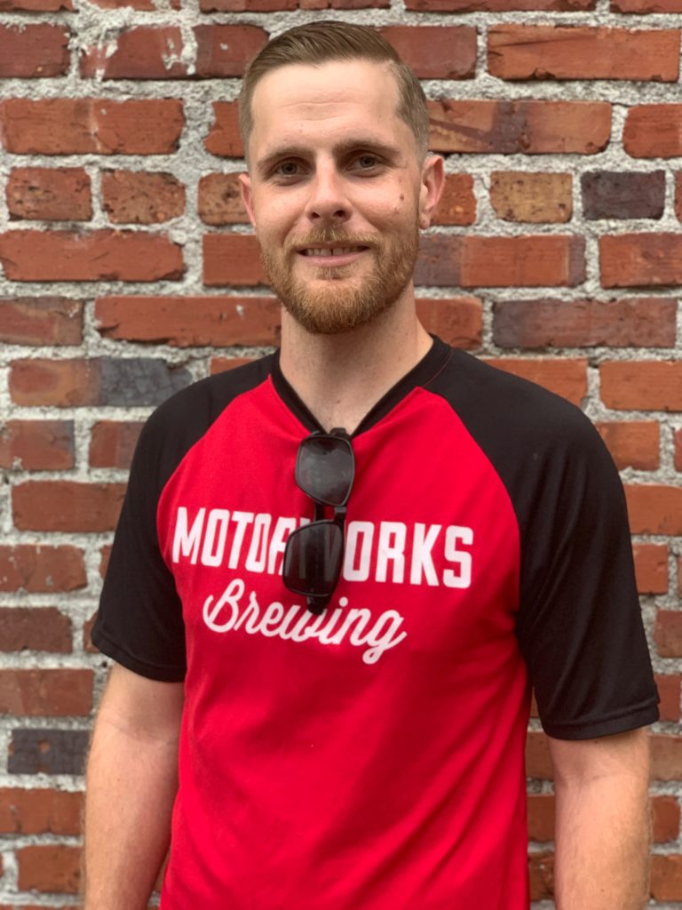 Motorworks Brewing Crew Photo - Zak Butcher trying not to smile in front of the brick wall