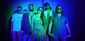 Motorworks Brewing presents Tropico BLVD band members dressed in tropical clothes in center of blue lit image and dark corners